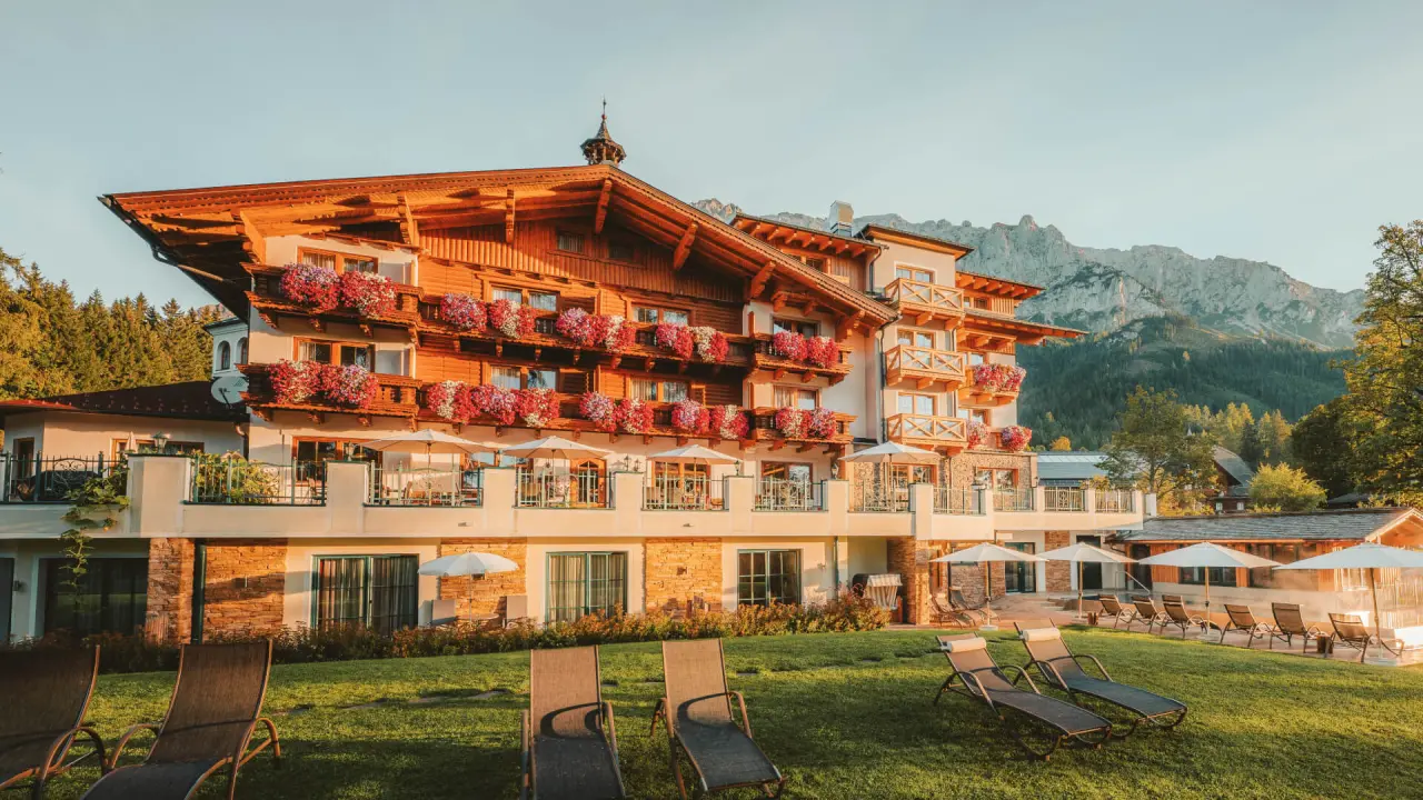 Traditionelles Hotel Lindenhof mit blumengeschmückten Balkonen, Sonnenterrasse und Alpenpanorama im Abendlicht.