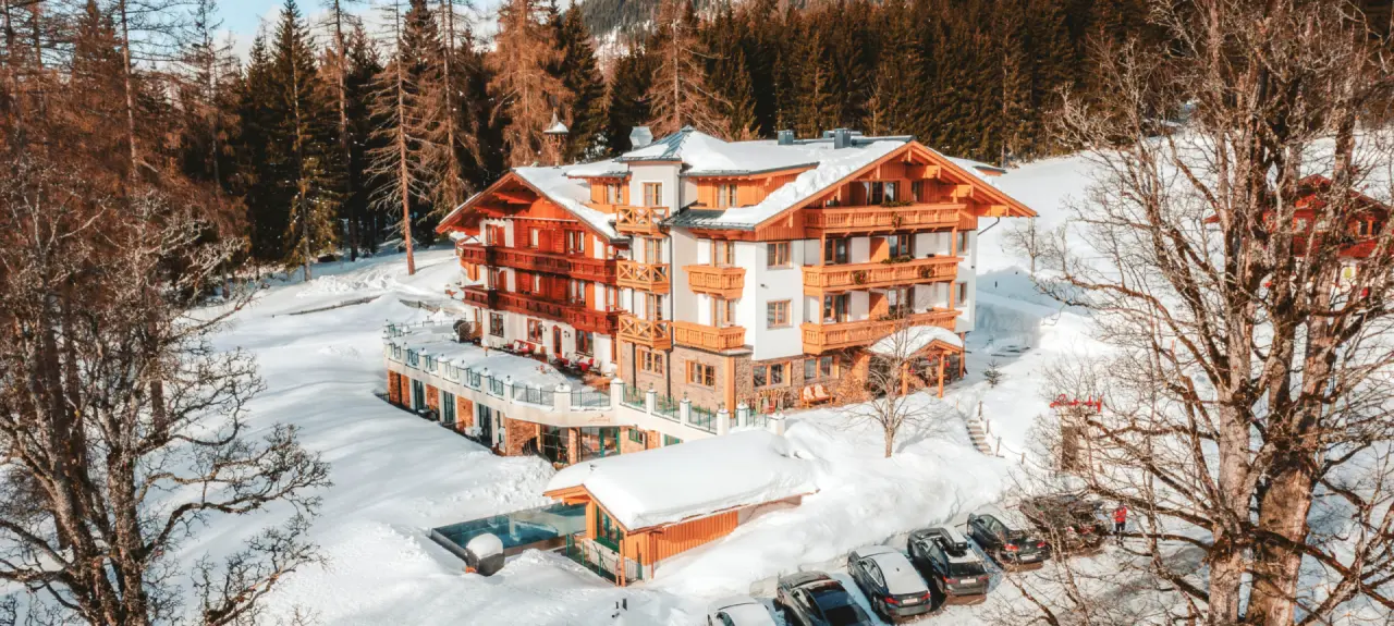 Winterliche Aussenansicht des Hotel Lindenhof mit verschneiter Landschaft, Wald und beheiztem Aussenpool.