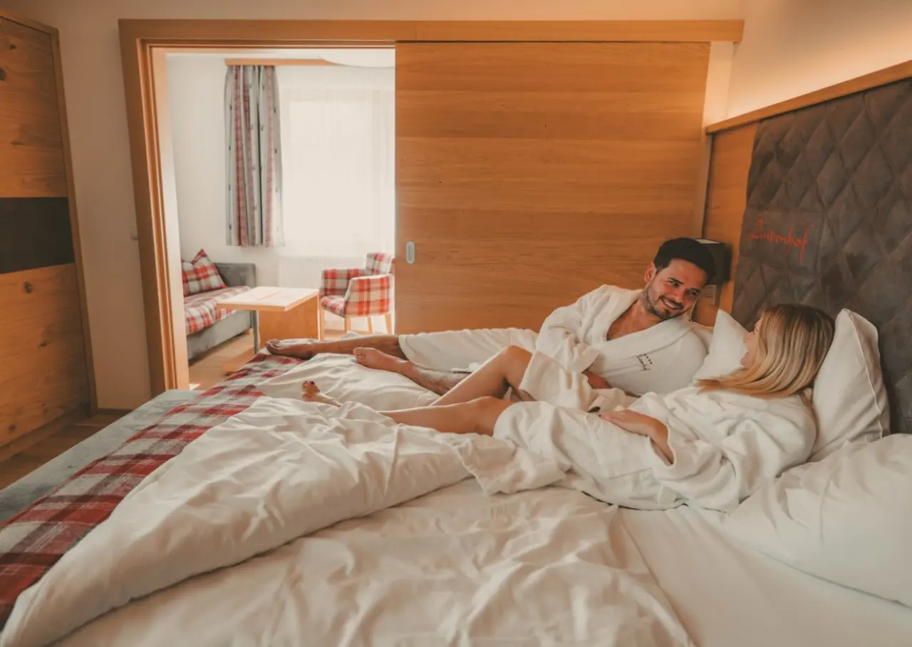 Entspanntes Paar in Bademänteln im komfortablen Hotelzimmer des Hotel Lindenhof mit angrenzendem Wohnbereich.