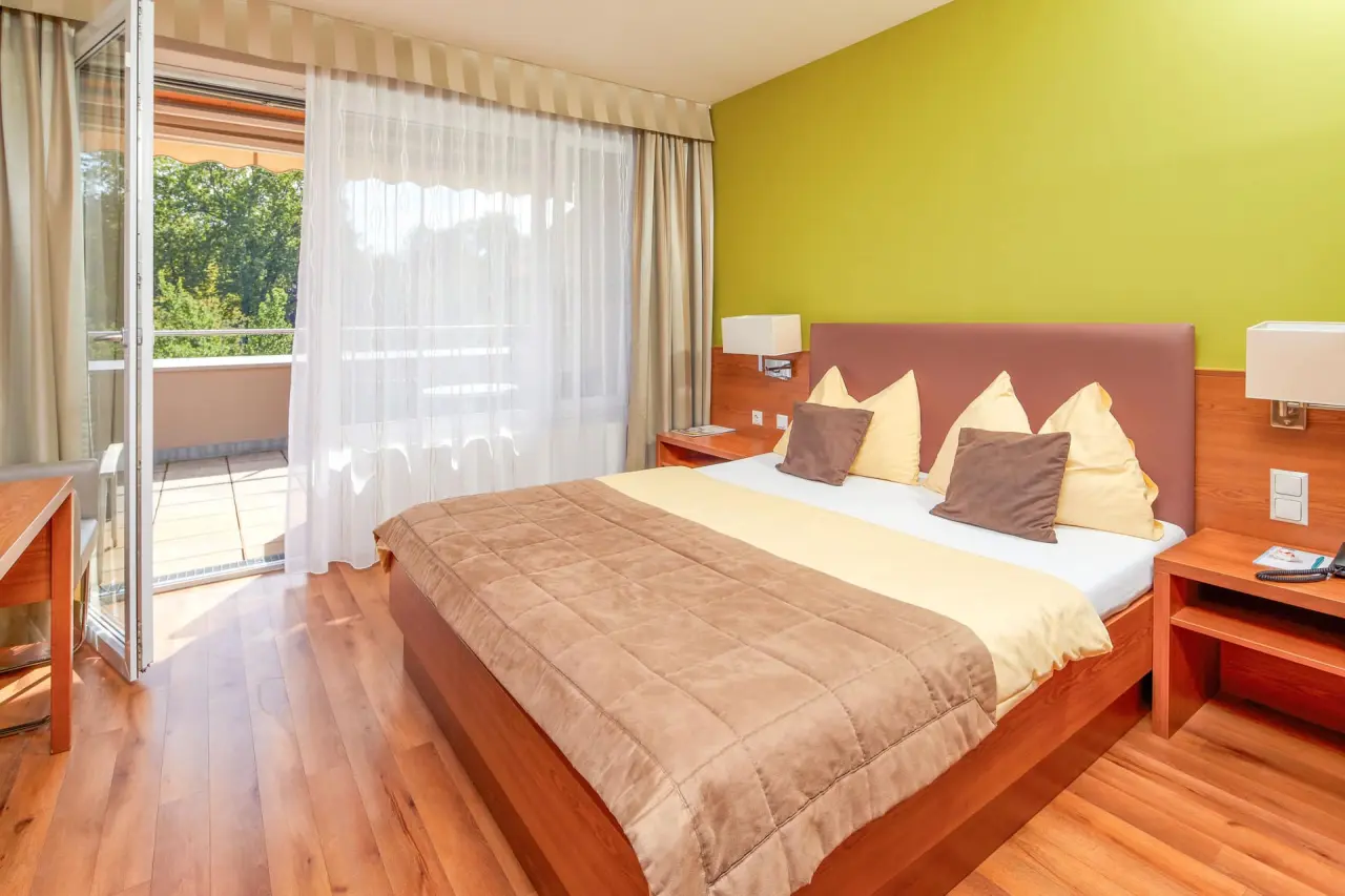 Helles Doppelzimmer mit Balkon und Blick ins Grüne im Thermalhotel Fontana.