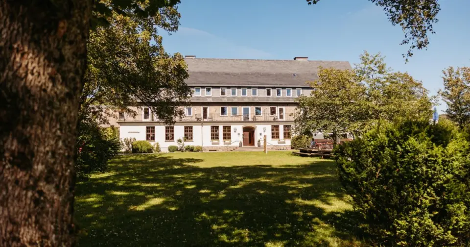 Idyllische Aussenansicht des Berghotels Hoher Knochen mit weitläufiger Grünfläche und Bäumen im Sauerland.