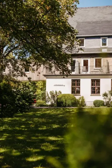 Aussenansicht des Berghotels Hoher Knochen mit grüner Gartenanlage und Bäumen an einem sonnigen Tag.
