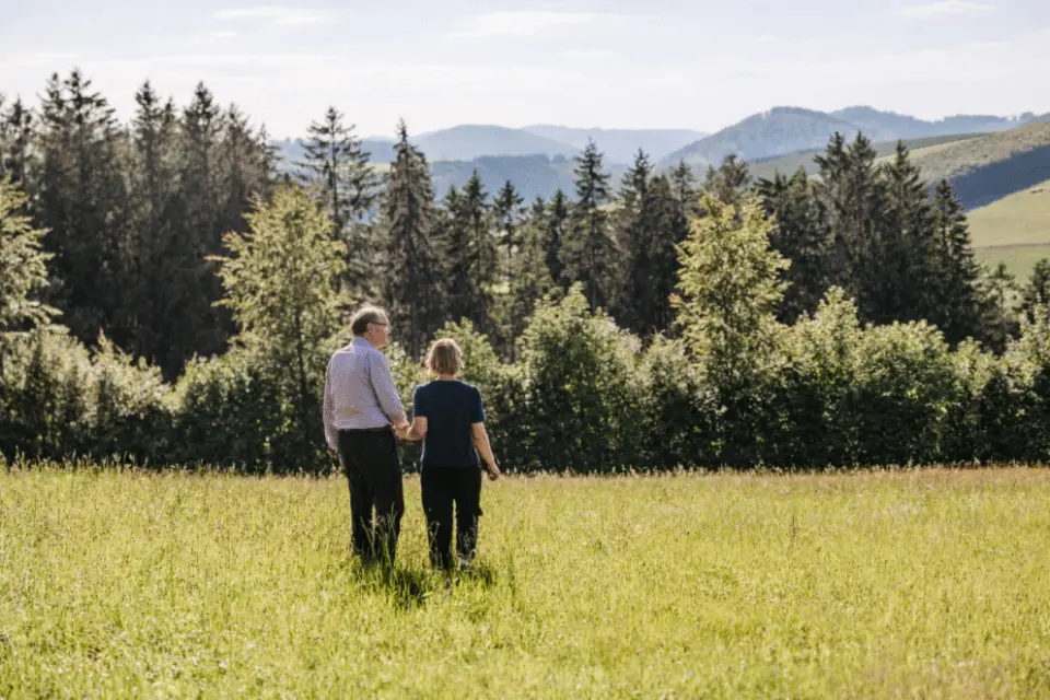 Paar spaziert Hand in Hand auf einer Bergwiese mit Wald und Panoramablick im Berghotel Hoher Knochen.
