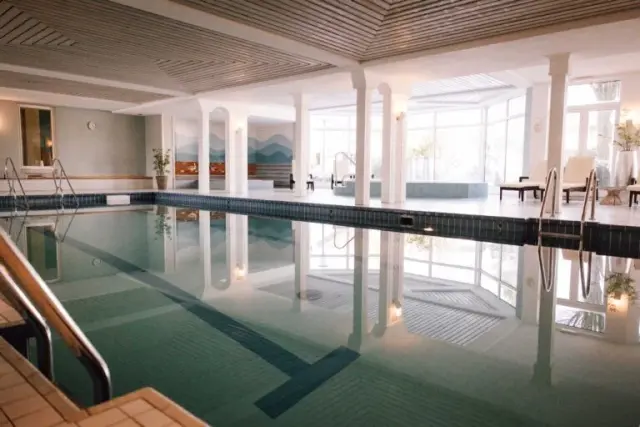 Geräumiger Innenpool mit großer Fensterfront und Liegestühlen im Wellnessbereich des Berghotel Hoher Knochen.