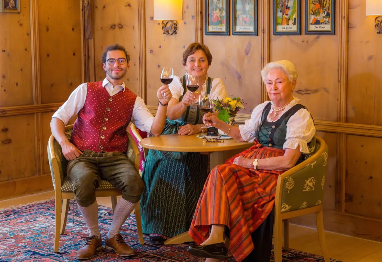 Drei Personen in Tracht stoßen mit Rotwein an im traditionellen Ambiente des Appart- und Wellnesshotel Charlotte Seefeld.
