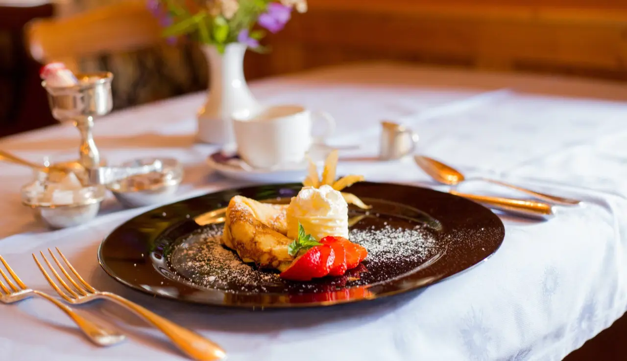 Dessert mit Palatschinken, Sahne und Erdbeeren auf einem Tisch im Restaurant des Appart- und Wellnesshotel Charlotte Seefeld.