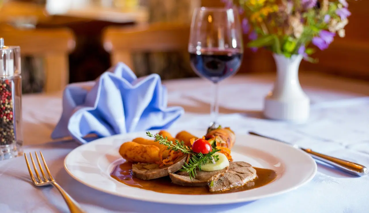 Appetitlich angerichtetes Gericht mit Fleisch, Kroketten und Rotwein im Restaurant des Appart- und Wellnesshotel Charlotte Seefeld.