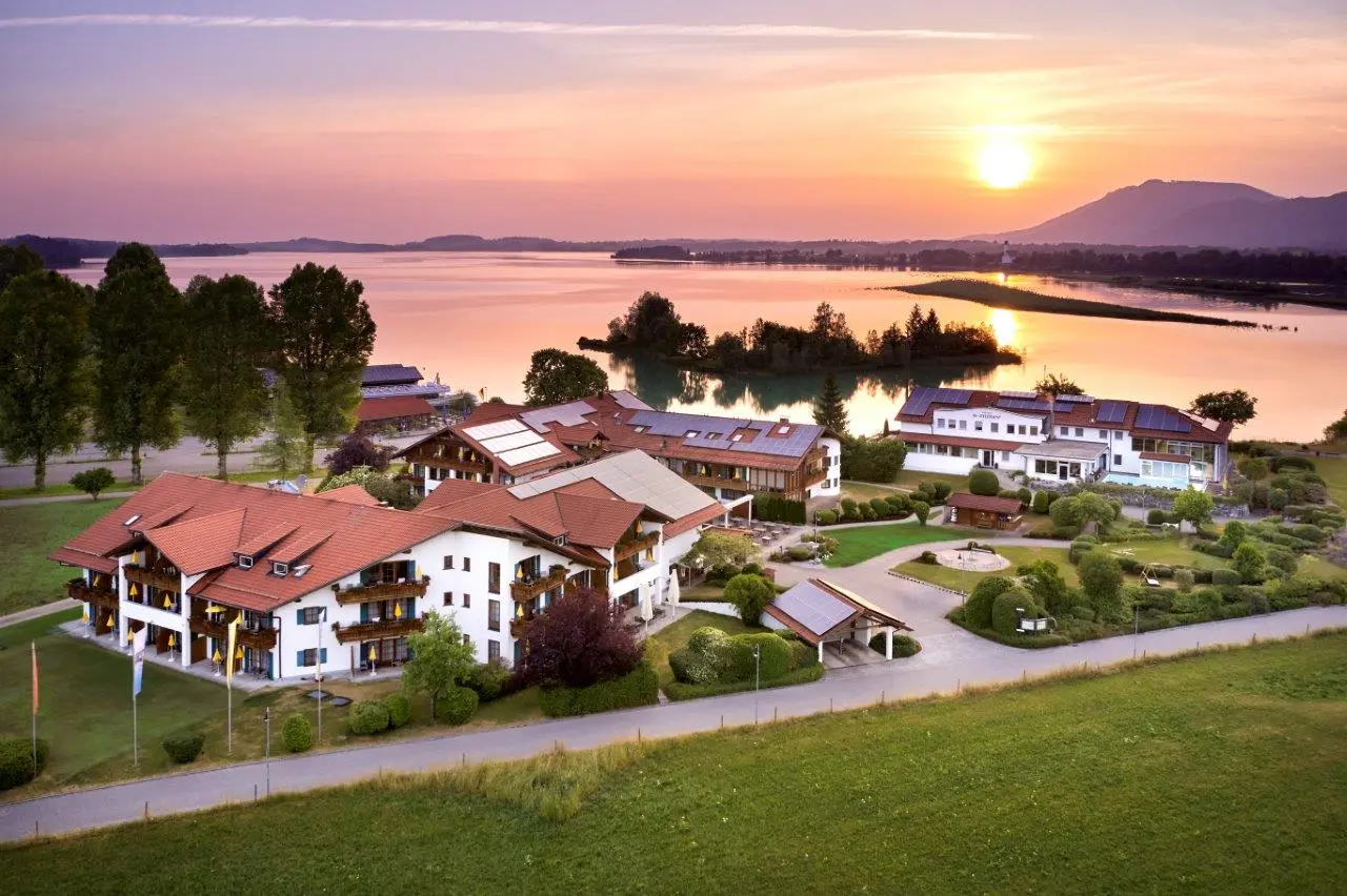 Luftaufnahme vom Hotel Sommer am Forggensee bei Sonnenuntergang mit Alpenpanorama im Hintergrund.