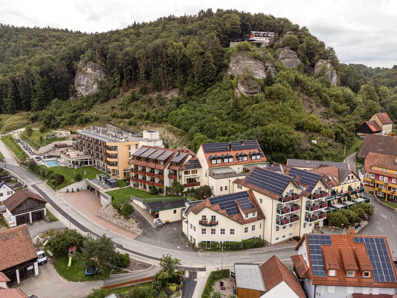 Luftaufnahme des Landhaus Sponsel-Regus mit Hotelgebäuden, Aussenpool und bewaldeter Hügellandschaft.