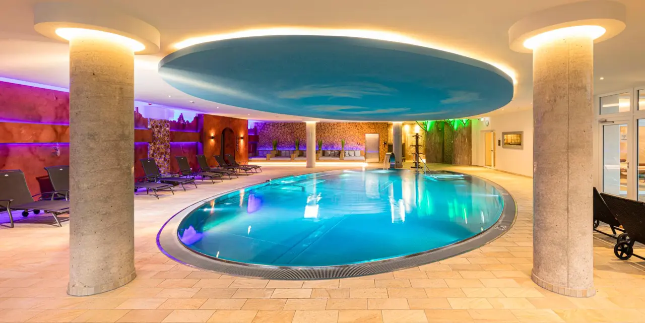 Einladender Innenpool mit stimmungsvoller Beleuchtung und Liegebereich im Wellnessbereich des Landhaus Sponsel-Regus.