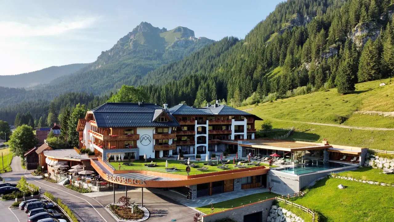 Aussenansicht des 5-Sterne Hotel Bergblick mit Infinity Pool, Sonnenterrasse und majestätischem Bergpanorama in den Alpen.