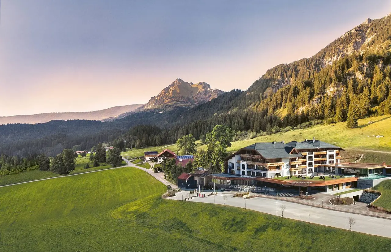 Panoramablick auf das 5-Sterne Hotel Bergblick, eingebettet in die malerische Alpenlandschaft mit grünen Wiesen.