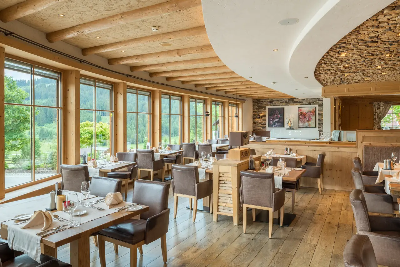Helles Restaurant im Hotel Bergblick mit Holzelementen, elegant gedeckten Tischen und Panoramablick auf die Natur.