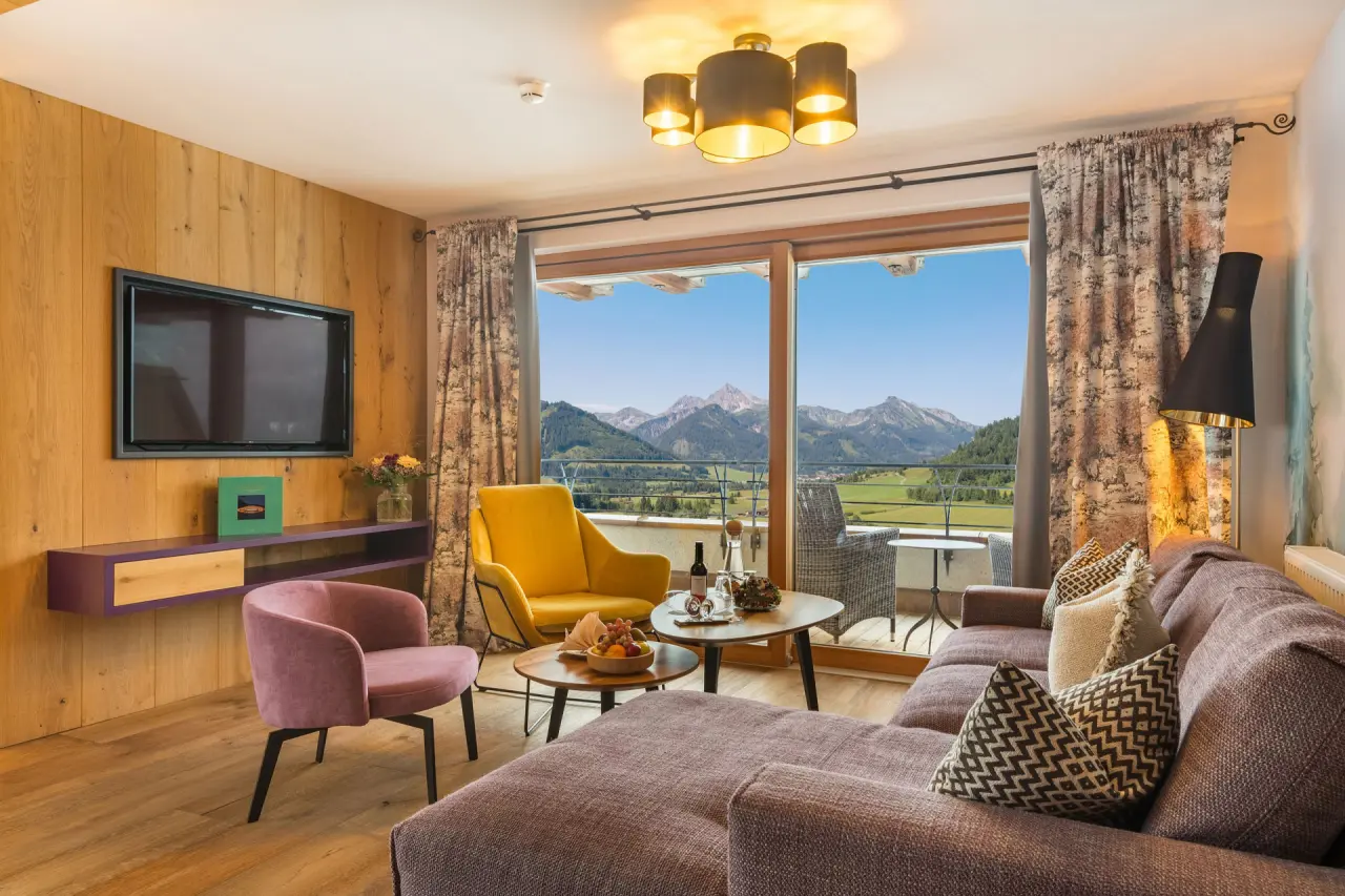 Geräumige Hotelsuite im Hotel Bergblick mit gemütlicher Sitzecke, TV und Balkon mit atemberaubendem Alpenpanorama.