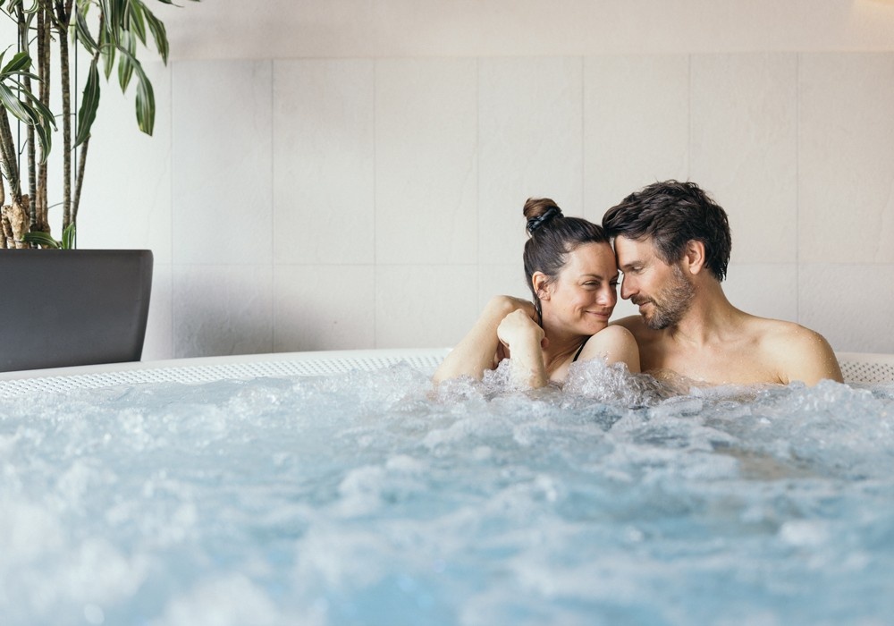 Hotel Kaiserblick in Ellmau – Glückliches Paar entspannt im sprudelnden Whirlpool des Wellnessbereichs | Wellnesshotel Tirol