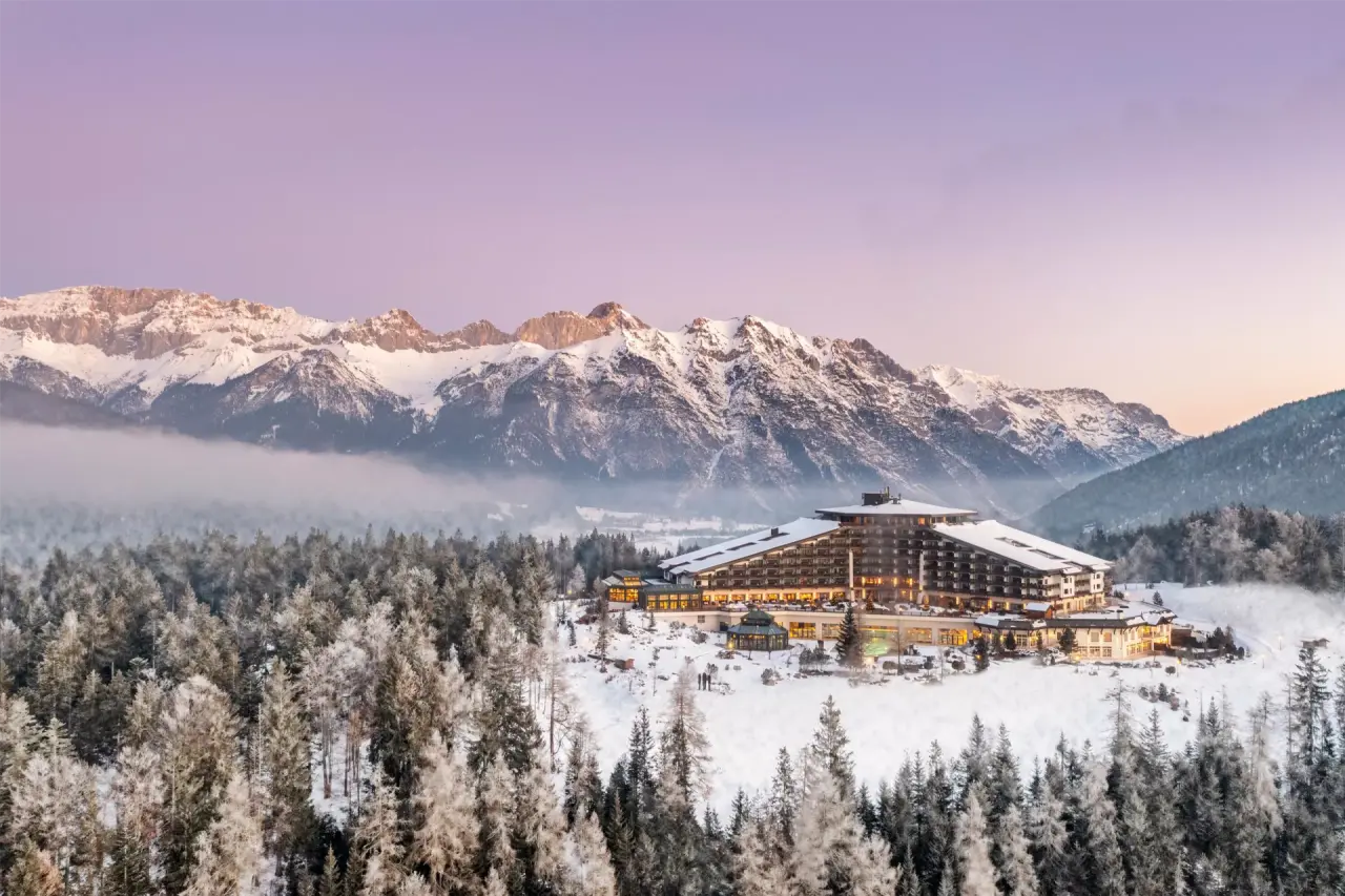 Majestätisches Interalpen-Hotel Tyrol im Winter, umgeben von verschneiten Alpen und Wäldern bei Dämmerung.