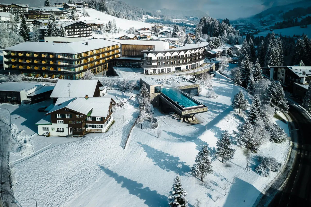 Luftaufnahme des Travel Charme Ifen Hotels im Winter mit schneebedeckter Landschaft und beheiztem Infinity Pool.