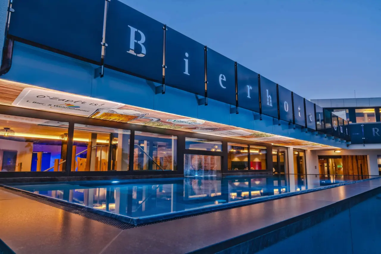 Beheizter Aussenpool bei Dämmerung mit beleuchtetem 'Bierhotel' Schriftzug im 1. Bier- und Wohlfühlhotel Gut Riedelsbach.