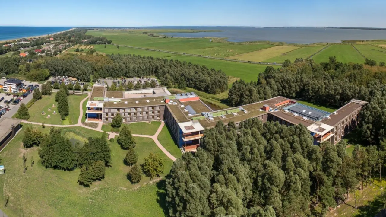 Luftaufnahme des Ostseehotel Dierhagen zwischen Ostsee und Bodden, umgeben von Wald und Wiesen unter blauem Himmel.