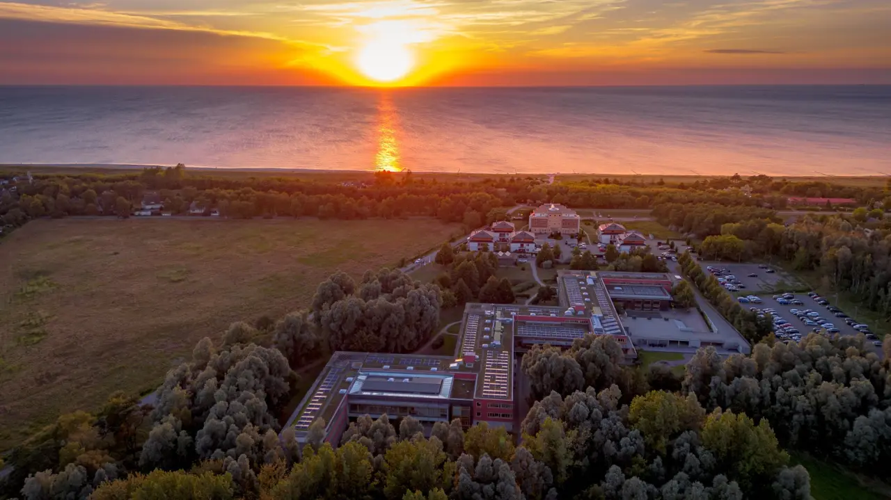 Luftaufnahme des Ostseehotel Dierhagen bei Sonnenuntergang über der Ostsee, umgeben von grüner Natur.