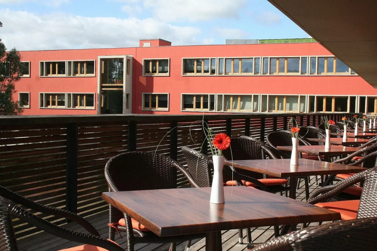 Außenbereich des Restaurants mit Tischen, Korbstühlen und Blick auf das moderne Ostseehotel Dierhagen.
