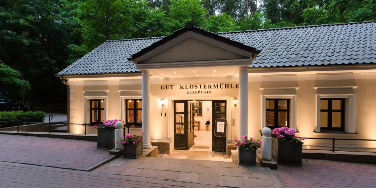 Beleuchteter Eingangsbereich der Rezeption im Gut Klostermühle Alt Madlitz mit Blumen bei Abenddämmerung.