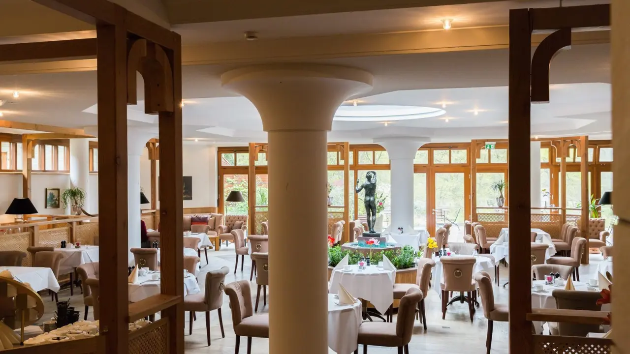 Helles Restaurant im Gut Klostermühle Alt Madlitz mit eleganten Tischen, bequemen Stühlen und dekorativer Statue.