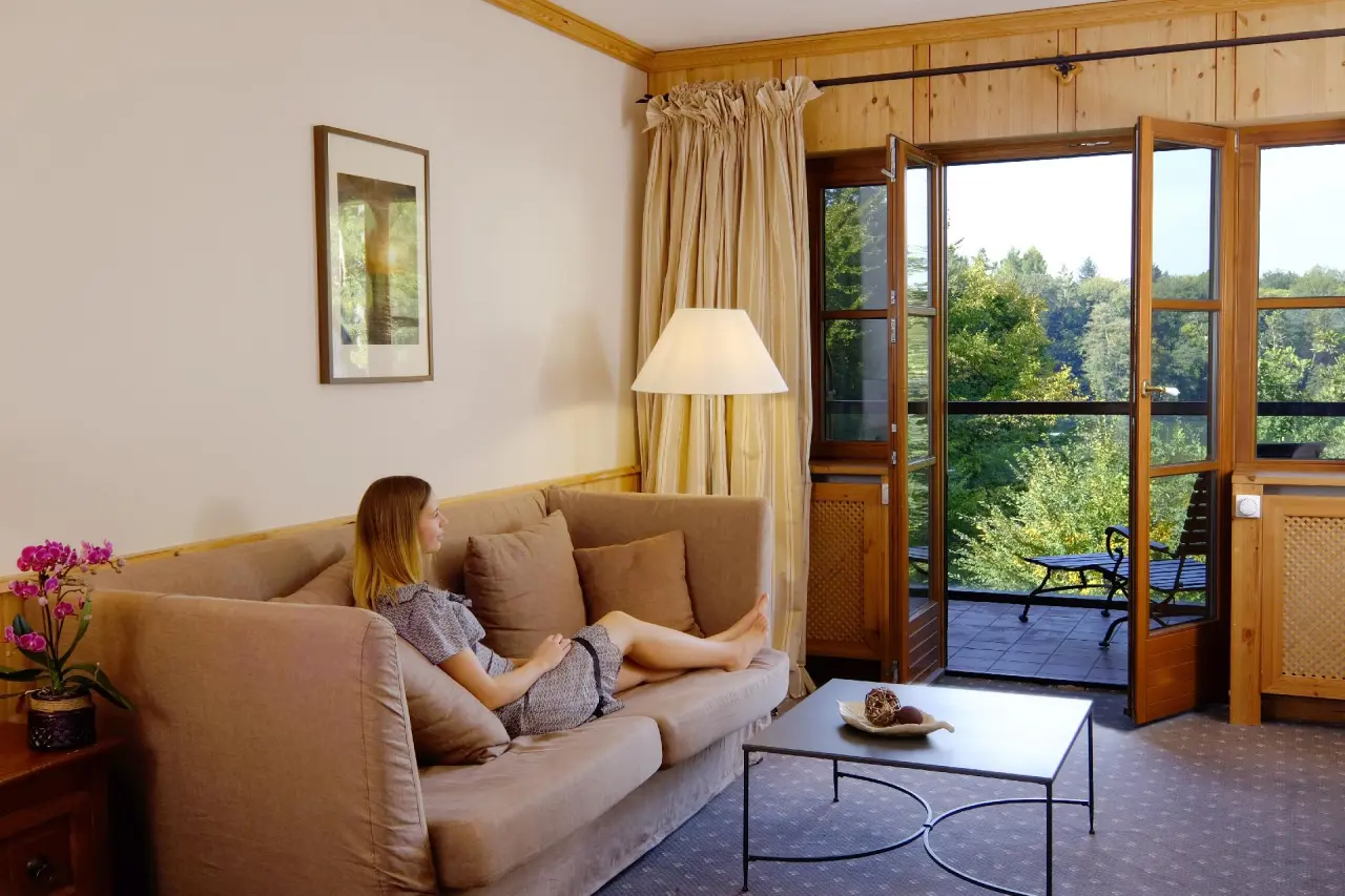 Gemütliches Hotelzimmer im Gut Klostermühle Alt Madlitz mit Balkon, Sofa und Blick auf den Wald.
