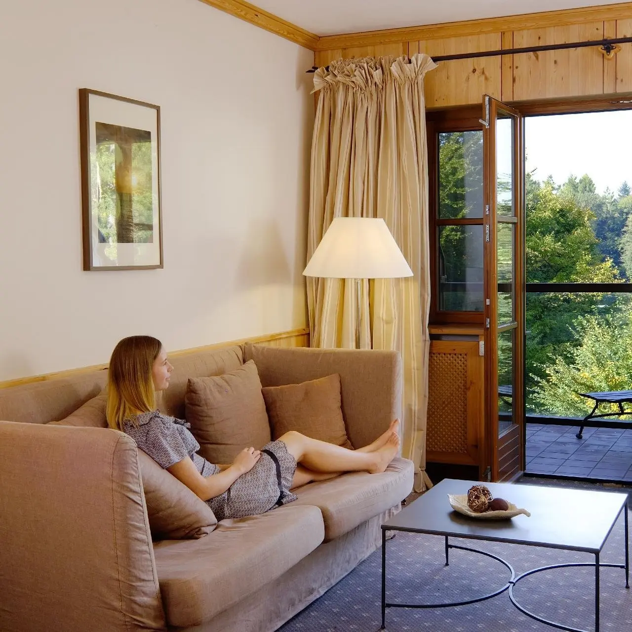 Gast entspannt auf dem Sofa im gemütlichen Hotelzimmer mit Balkon und Waldblick im Gut Klostermühle Alt Madlitz