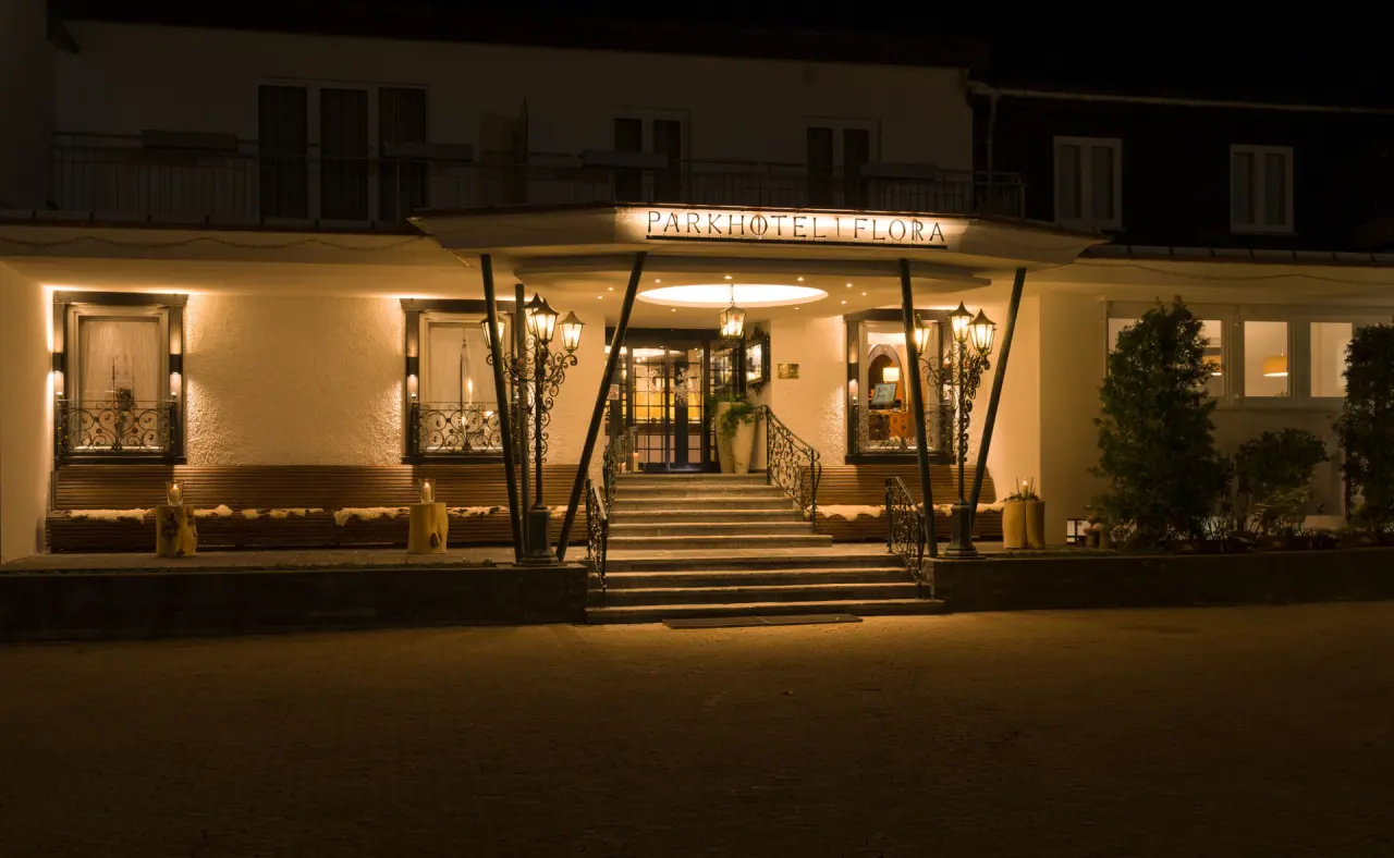 Einladender, beleuchteter Eingang des Parkhotel Flora bei Nacht mit Treppe und schmiedeeisernen Laternen.