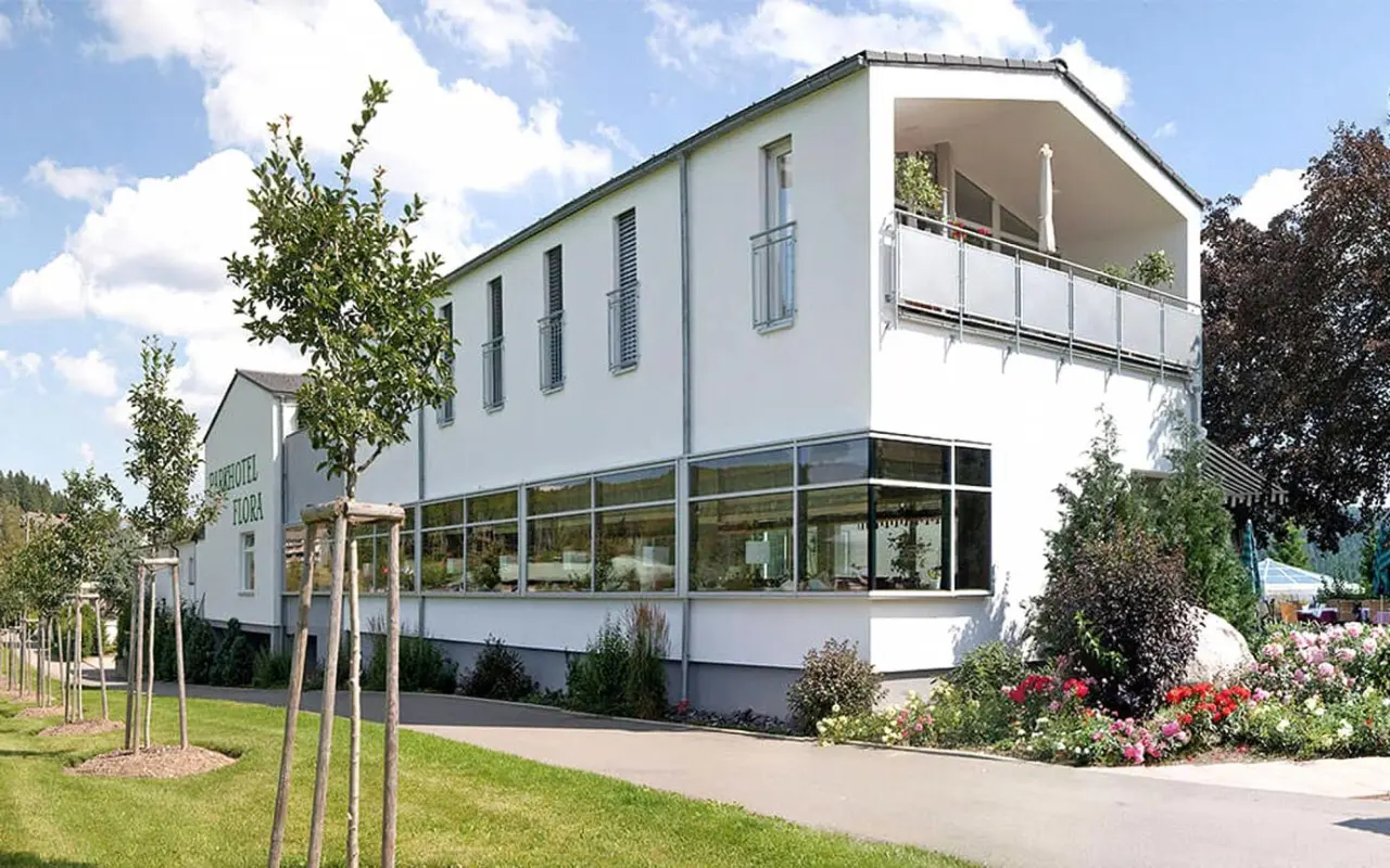 Moderne Aussenansicht des Parkhotel Flora mit weisser Fassade, grossen Fenstern, Balkon und gepflegtem Gartenbereich.