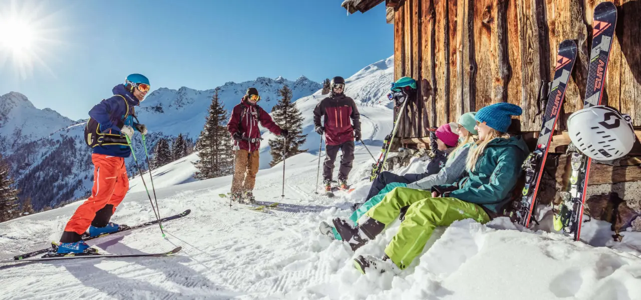 Skifahrer und Freunde entspannen vor einer Berghütte im sonnigen Schnee der Alpenregion beim Hotel Wastlhof.