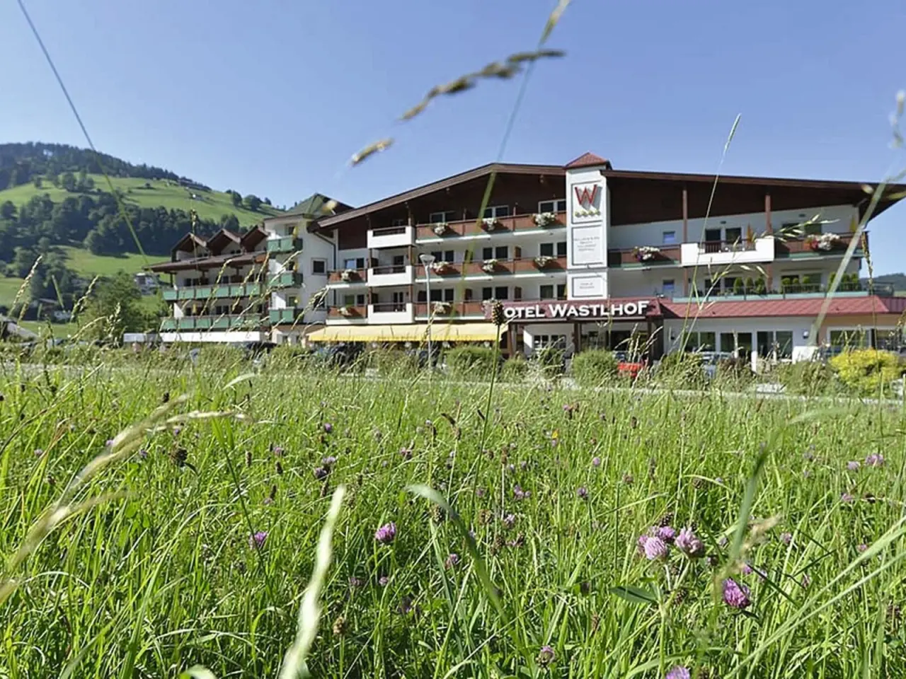 Aussenansicht des Hotel Wastlhof mit grüner Wiese und Bergen im Hintergrund an einem sonnigen Tag.