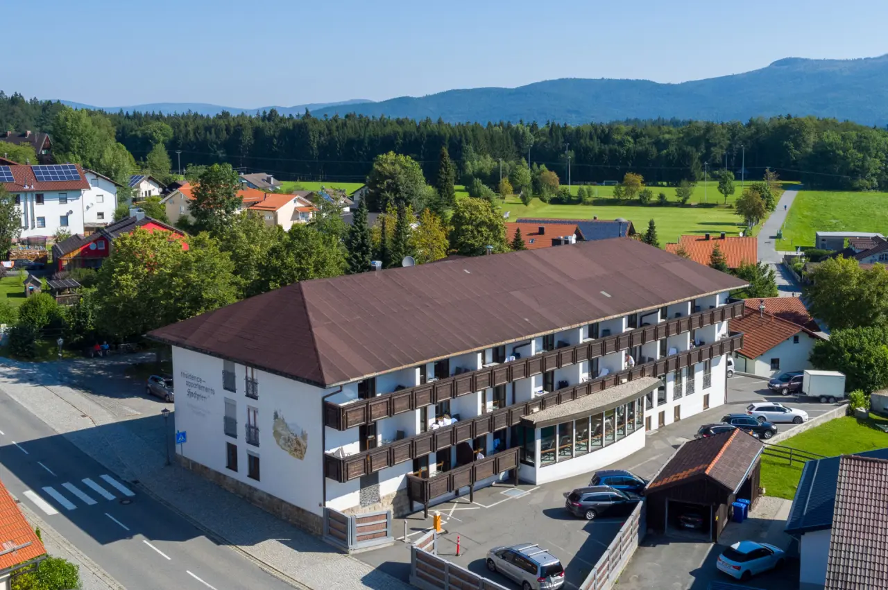 Aussenansicht des Hotel & Residence Hochriegel in sonniger Landschaft mit Balkonen, Wald und Bergen im Hintergrund.