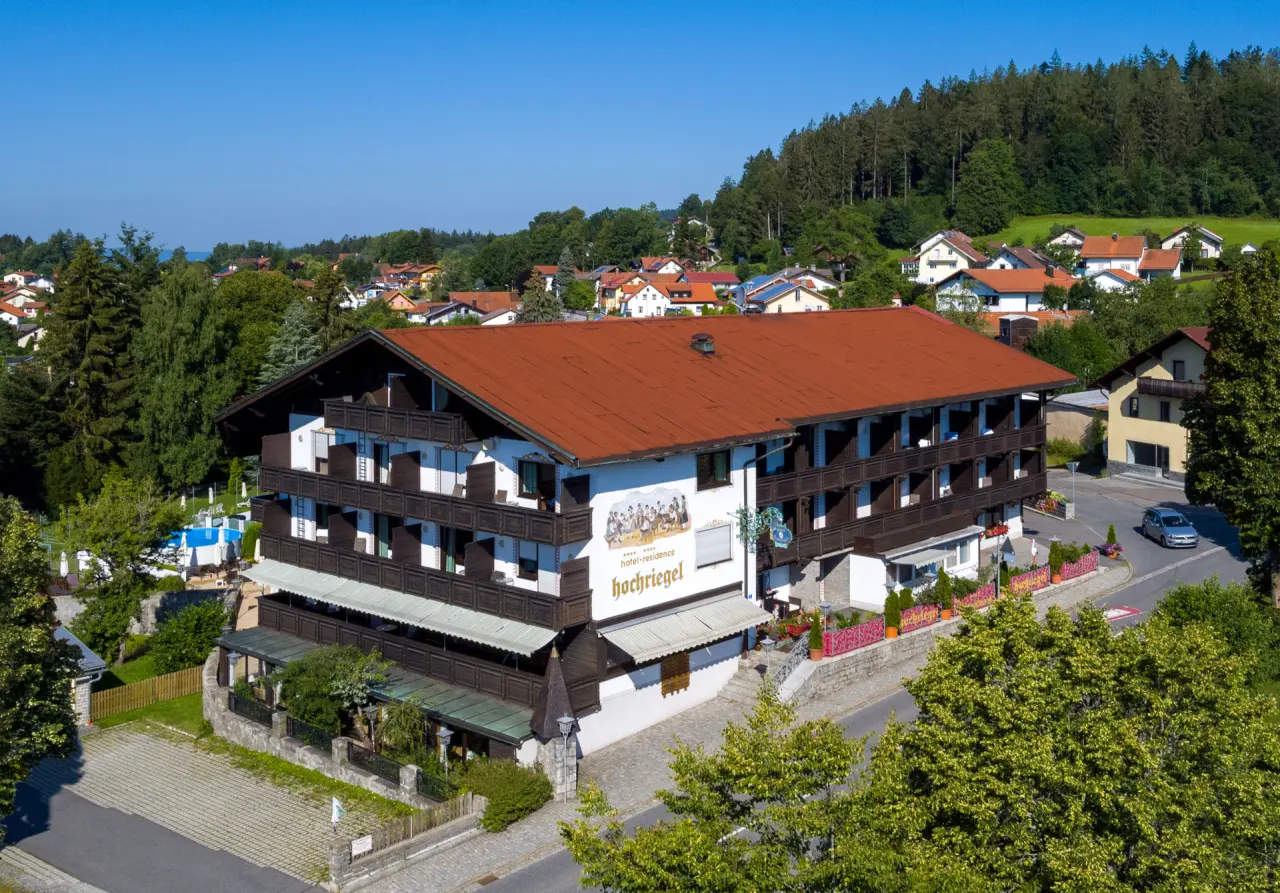 Luftaufnahme des Hotel & Residence Hochriegel im bayerischen Stil mit Balkonen und Aussenpool, umgeben von Gruen und Haeusern.