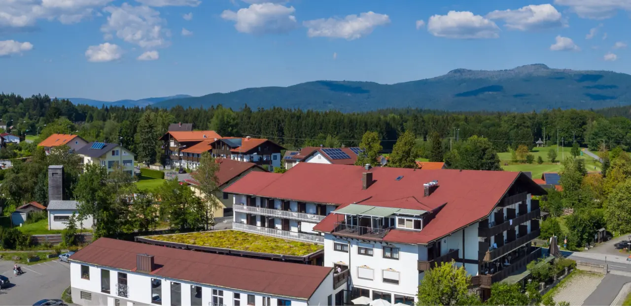 Luftaufnahme des Hotel & Residence Hochriegel mit roten Dächern, umgeben von grünen Wäldern und Bergen unter blauem Himmel.