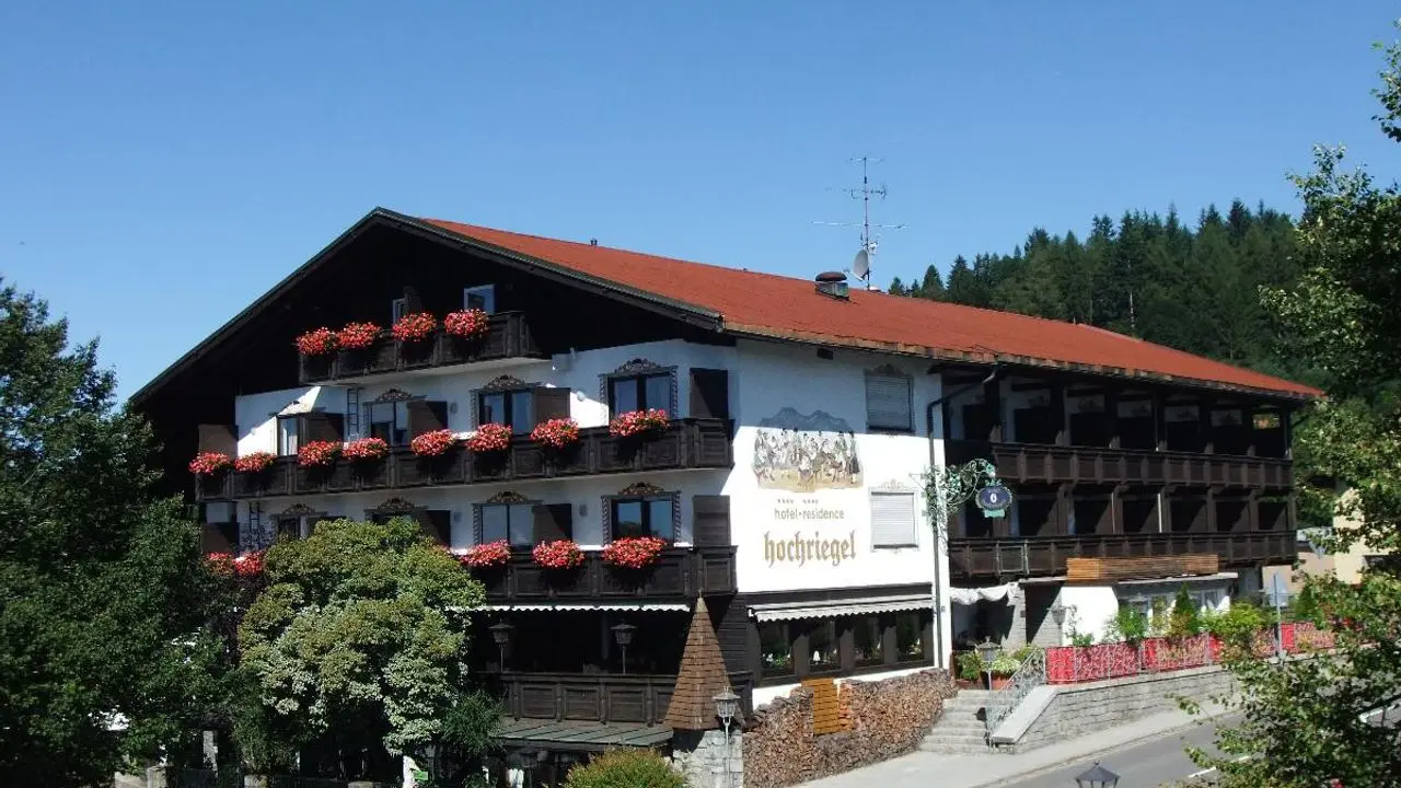 Traditionelles Hotel & Residence Hochriegel in den Bergen mit blühenden Balkonen und Wald im Hintergrund.