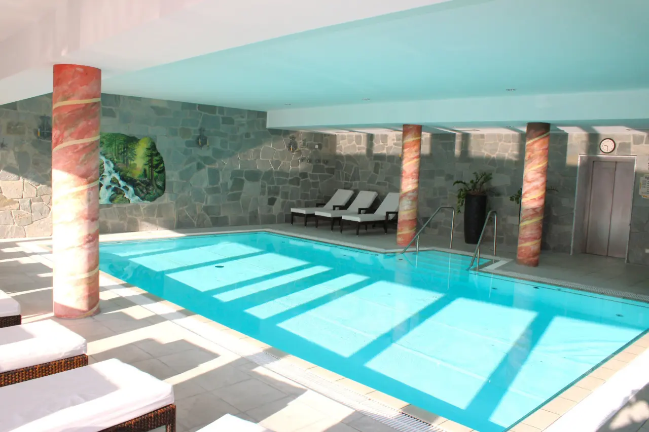 Grosser Innenpool mit Tageslicht, Liegen und Steinwand im Hotel & Residence Hochriegel