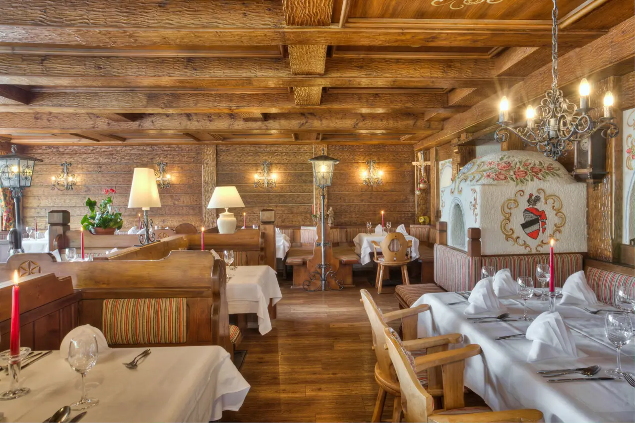 Gemütliches Restaurant im alpinen Stil mit Holzeinrichtung, festlich gedeckten Tischen und Kachelofen im Hotel & Residence Hochriegel.
