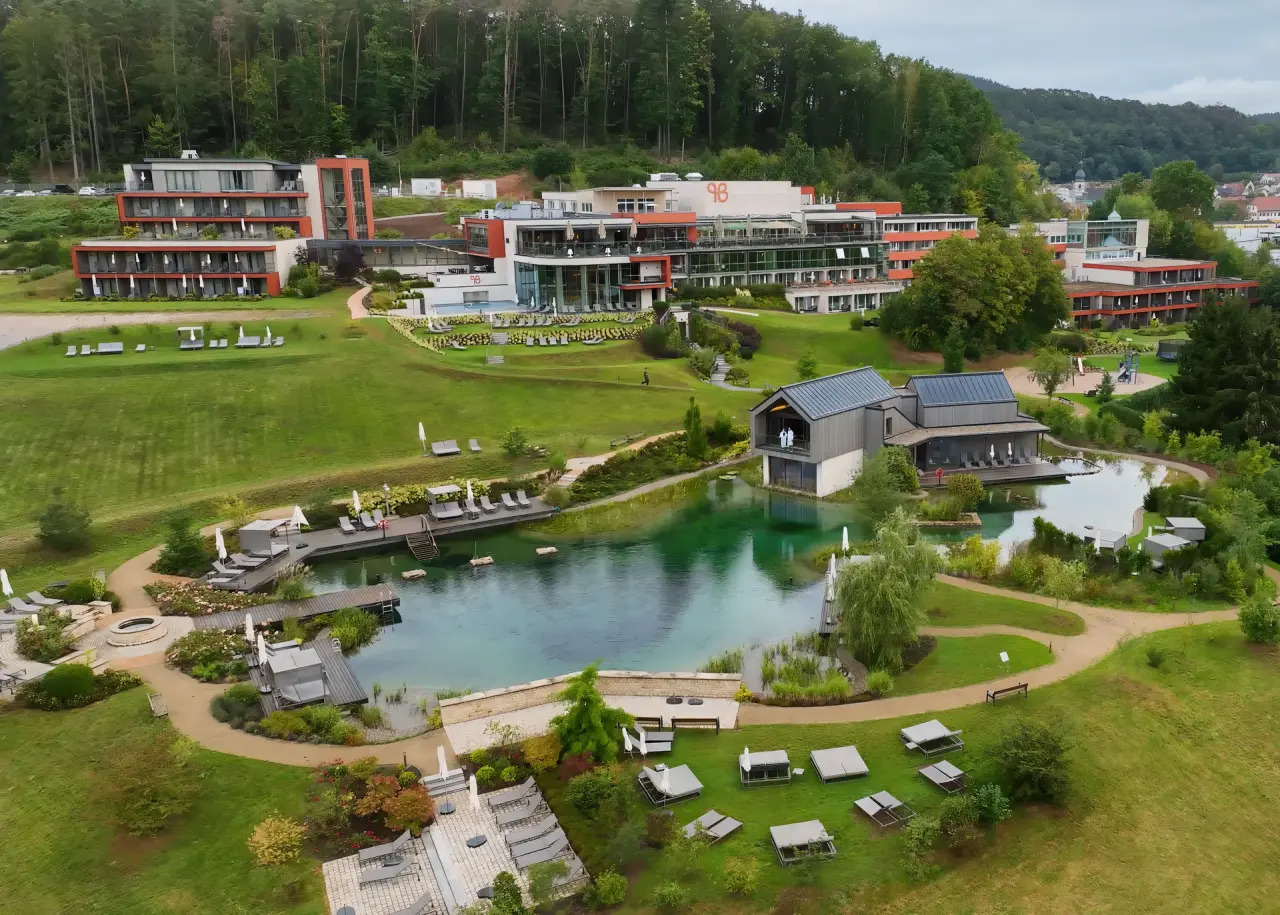 Pfalzblick Wald Spa Resort: Luftaufnahme des weitläufigen Resorts mit Natur-Badeteich, modernen Gebäuden und Waldkulisse.