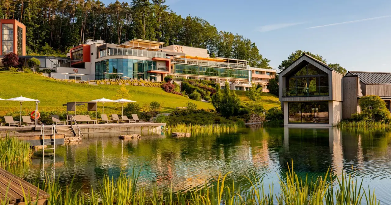 Panoramablick auf das Pfalzblick Wald Spa Resort mit Natursee, Liegewiese und moderner Architektur im Grünen.