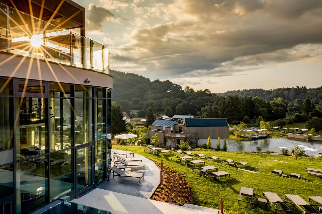Pfalzblick Wald Spa Resort: Moderne Spa-Architektur, weitläufige Liegewiese und Natur-Badeteich im Abendlicht.