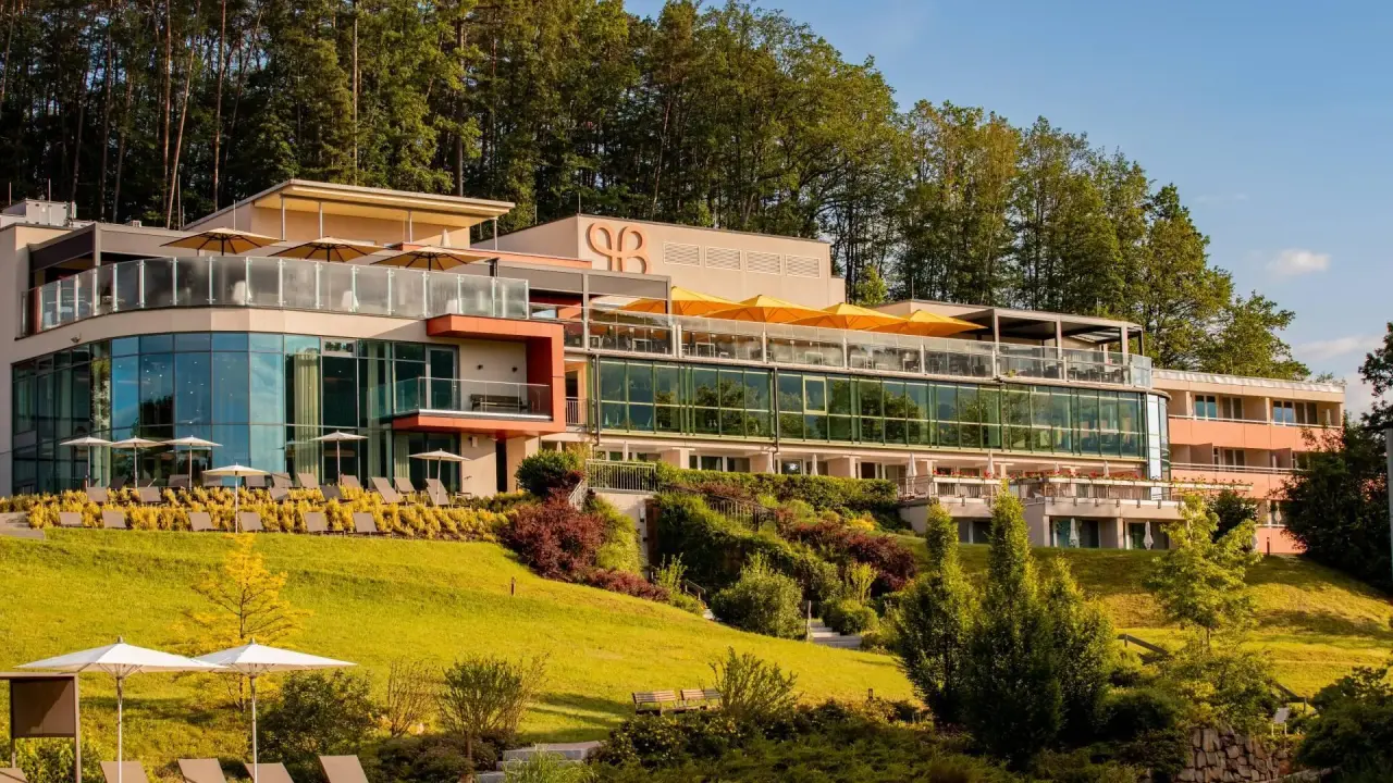 Aussenansicht des Pfalzblick Wald Spa Resort mit modernen Gebäuden, grünen Terrassen und Waldkulisse.