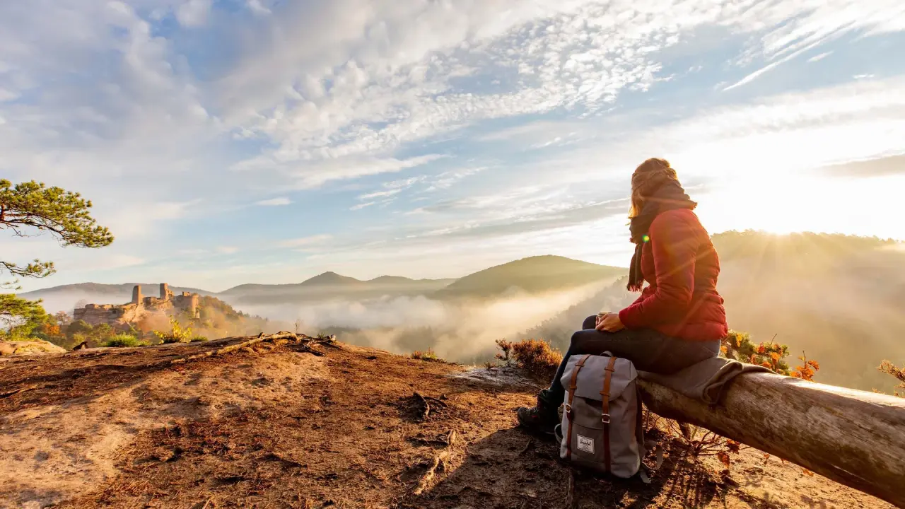 Wanderin genießt Sonnenaufgang über nebelverhangenem Tal mit Burgruine im Pfalzblick Wald Spa Resort Umgebung.