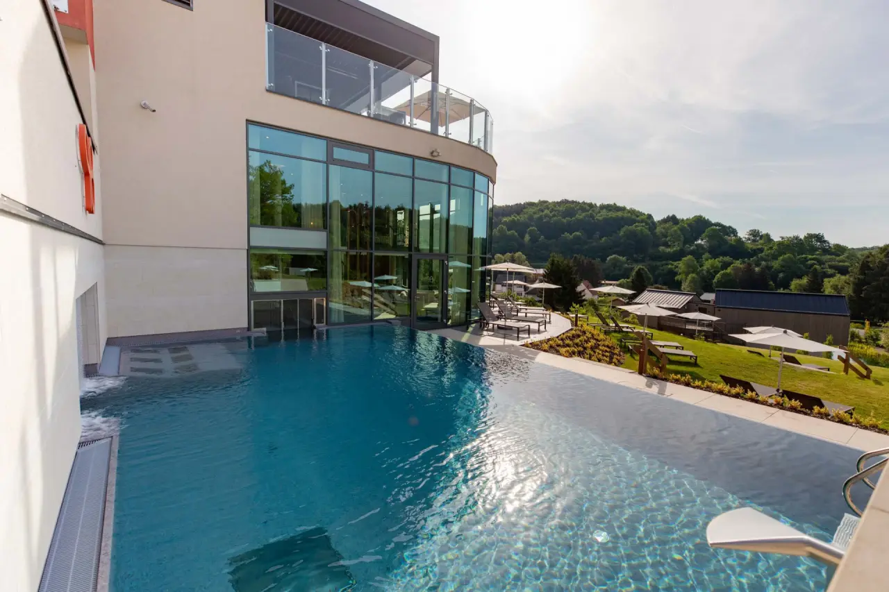 Grosszügiger Aussenpool mit Infinity-Rand und moderner Architektur des Pfalzblick Wald Spa Resort, umgeben von grüner Natur.