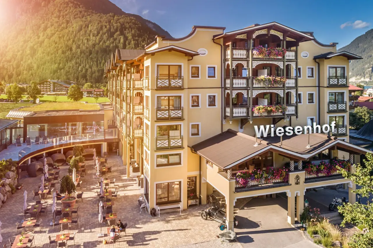 Malerische Aussenansicht des Hotel der Wiesenhof mit blühenden Balkonen und Bergpanorama im sonnigen Tal.