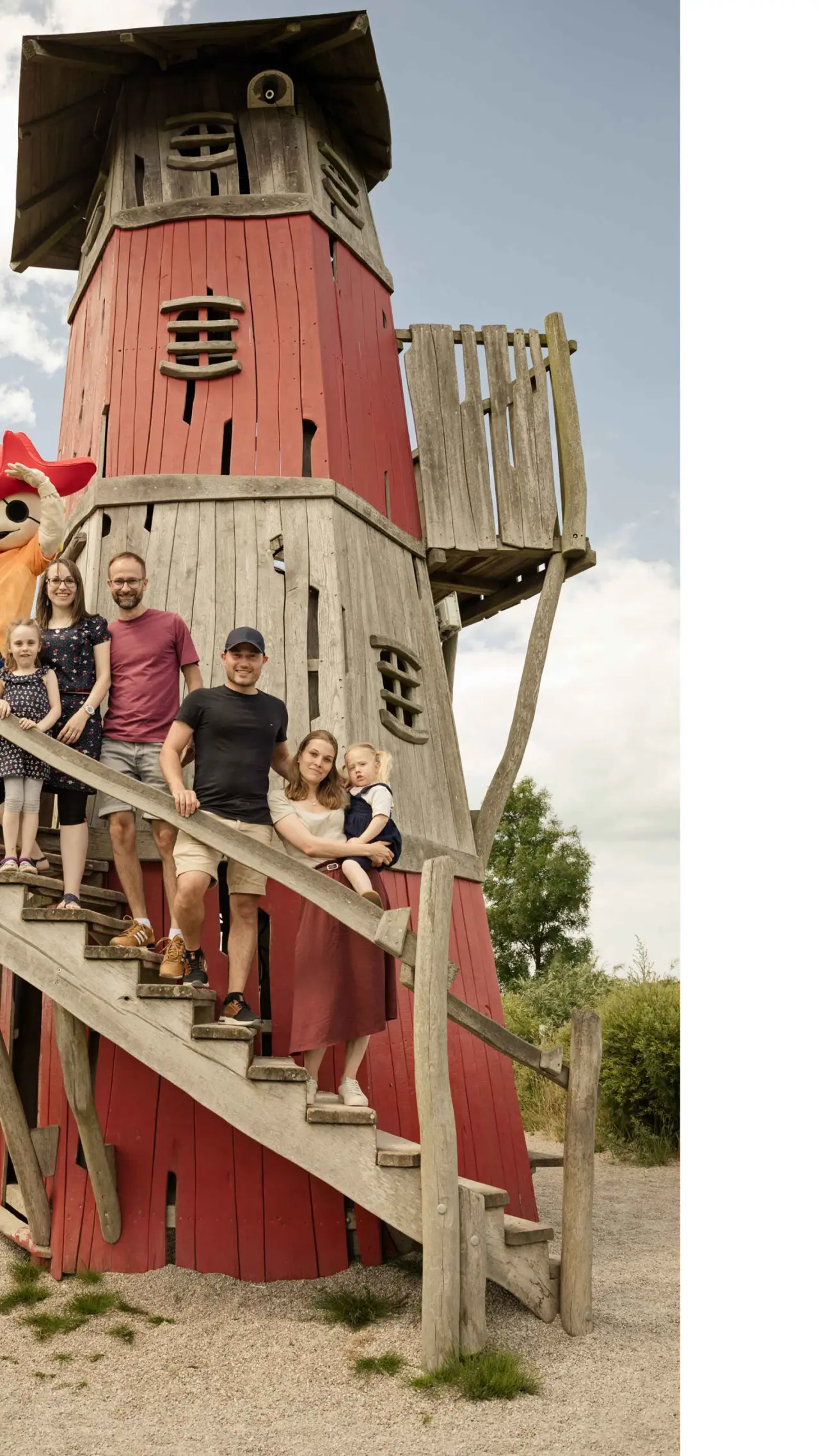 Familie mit Kindern und Hotelmaskottchen auf einem roten Holzturm im Aussenbereich des Familien Wellness Hotel Seeklause.