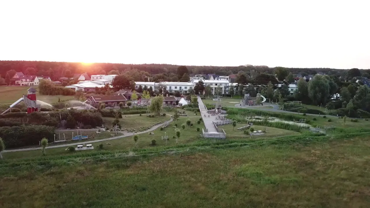 Luftaufnahme des Familien Wellness Hotel Seeklause bei Sonnenuntergang mit Hotelgebäude, großem Abenteuerspielplatz und Grünflächen.
