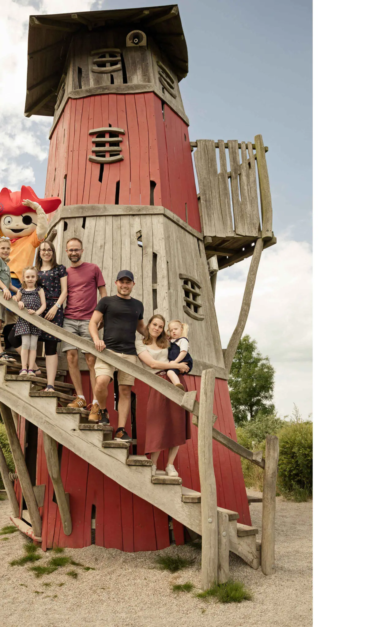 Familie mit Kindern und Hotelmaskottchen auf dem roten Leuchtturm-Spielplatz des Familien Wellness Hotel Seeklause.