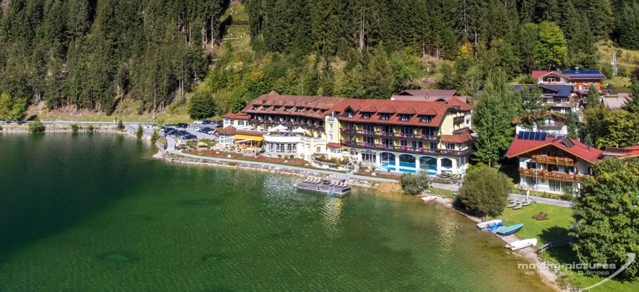 Panoramablick auf das Hotel Via Salina direkt am See mit Aussenpool und Liegebereich, umgeben von grünen Wäldern.